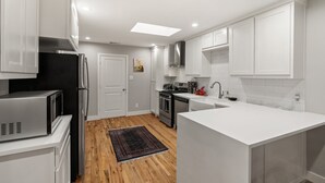 A modern kitchen with white cabinetry, stainless steel appliances, and a wooden floor. - Spacious 5BR Near Bishop Arts - 5 Min Drive! (Dallas)
