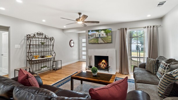 A living room with a fireplace, leather sofas, a coffee table, and a television mounted on the wall. - Spacious 5BR Near Bishop Arts - 5 Min Drive! (Dallas)