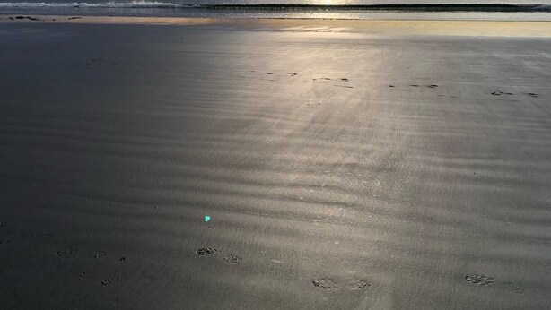 Uma praia com uma extensa faixa de areia e um mar calmo.