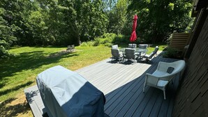 Um deck com móveis de exterior, incluindo cadeiras e uma mesa, rodeado por um deck de madeira e uma área gramada.