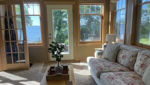 Ein Zimmer mit Meerblick, ein blumiges Sofa, ein Holztisch mit einer Vase und eine Tür mit Glasfeldern.