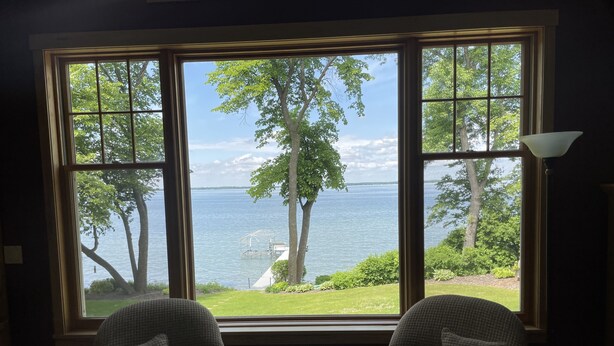 Ein Zimmer mit einem großen Fenster und Blick auf einen See und Bäume. Zwei Sessel befinden sich im Raum.
