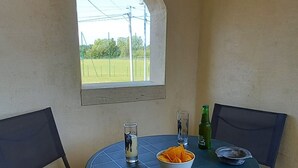 Una mesa redonda con un frutero y dos sillas, una ventana, y una botella sobre la mesa.