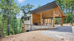 A modern cabin with a covered porch, surrounded by a forest. - Red Stag Ridge ~  Mtn Views ~ Hot Tub ~ EV Charger (Ellijay)