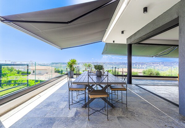 A modern outdoor dining area with a table and chairs, a large umbrella, and a view of the cityscape.