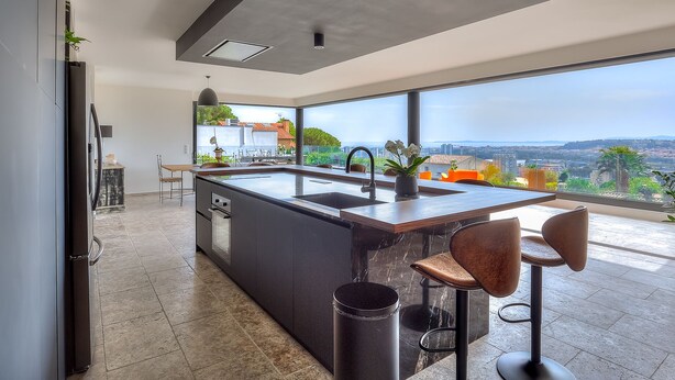 Une cuisine moderne dotée d’un grand îlot central, d’un évier et offrant une vue sur la ville.