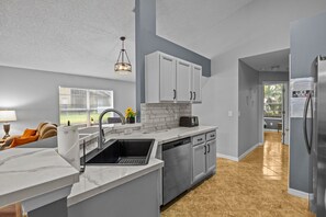 A modern kitchen with a marble countertop, stainless steel appliances, and a view to the outdoors.