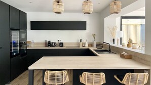 A modern kitchen with a large island, black cabinets, and three wicker chairs.