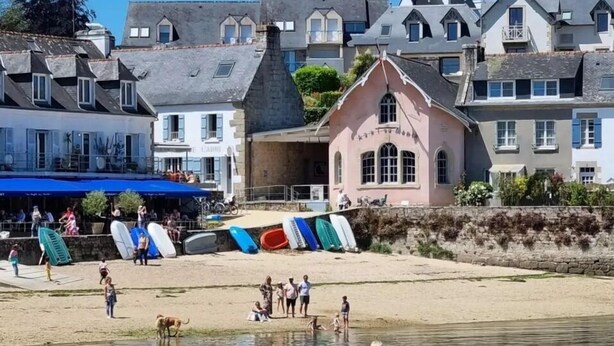 A coastal area with a sandy beach, a row of colorful kayaks, and a row of houses with distinct architectural styles.