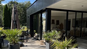 A modern outdoor patio area with potted plants, a pergola, and a stone pathway leading to a glass door entrance.