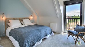 A bedroom with a bed, a chair, a radiator, and a balcony with a view. - Des deux plages - PLERIN (PLERIN)