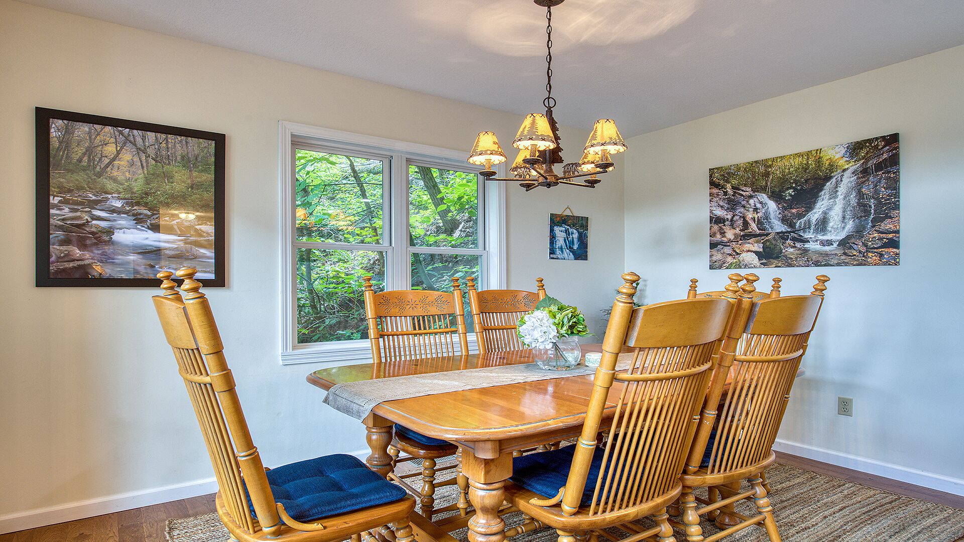 A dining area with a wooden table and chairs, a chandelier, and framed pictures on the walls.