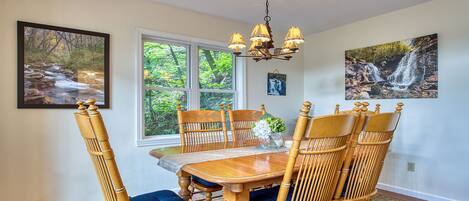 A dining area with a wooden table and chairs, a chandelier, and framed pictures on the walls.