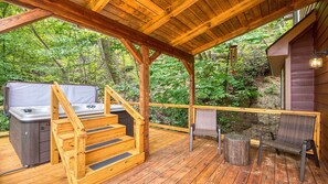 A wooden deck with a hot tub and steps leading to a covered area.