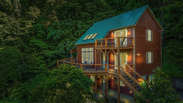 A two-story cabin with a balcony, surrounded by dense forest. - The Overlook /Hot Tub/Mountain Views/Babbling Creek/Fire Table (Maggie Valley)