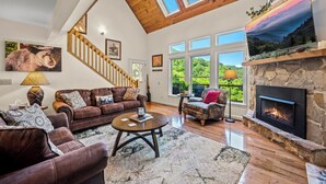 A spacious living room with a fireplace, large windows, and a wooden ceiling. - The Overlook /Hot Tub/Mountain Views/Babbling Creek/Fire Table (Maggie Valley)