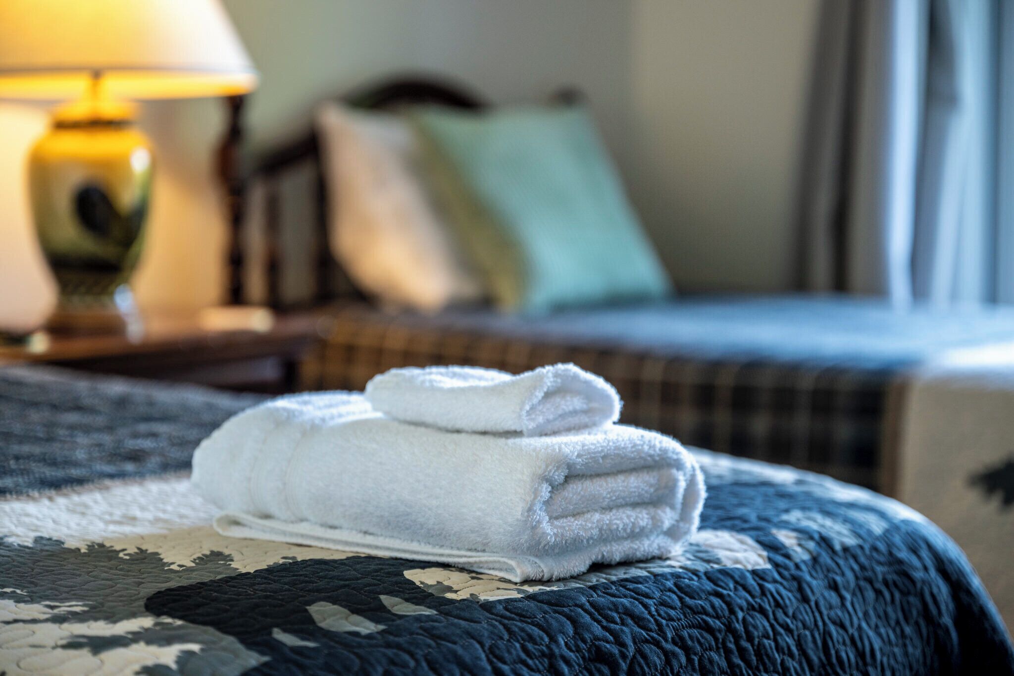 A neatly folded white towel on a bed with a dark blue quilt.
