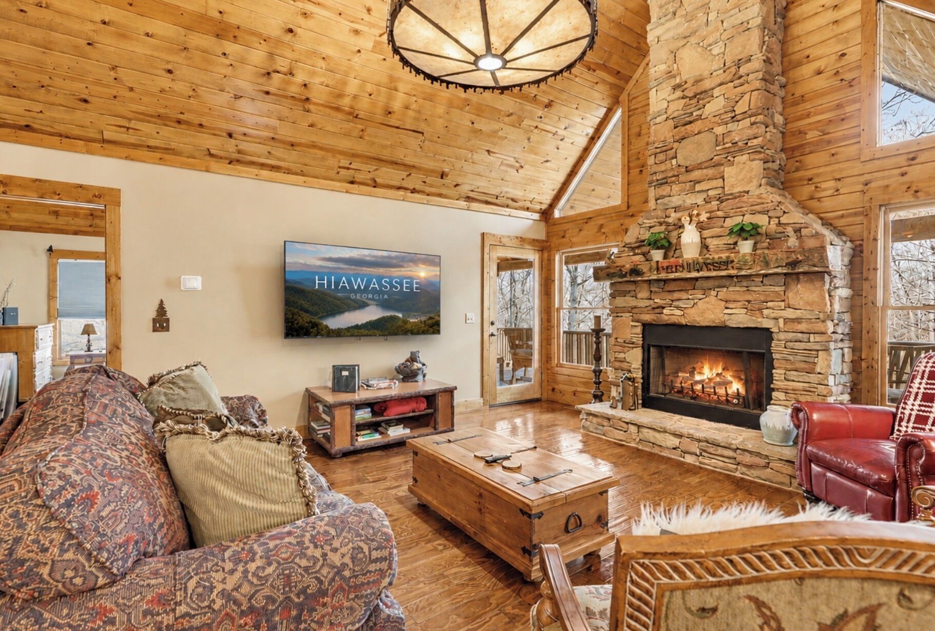 Interior acogedor de una cabaña con chimenea de piedra, paredes de madera, un televisor montado en la pared y una zona de estar cómoda con un sofá y un sillón rojo.