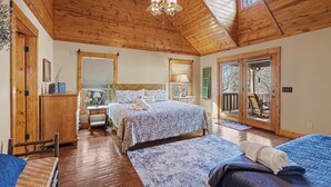 A spacious bedroom with two beds, wooden flooring, a ceiling fan, and a view through a glass door. - Vintage Luxury Creekside Cabin ~ King Bed, Hot Tub, Fire Pit & Game Room, Dog Ok (Hiawassee)