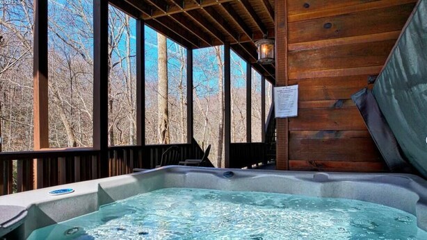 A hot tub in a wooden cabin with large windows overlooking a forest. - Vintage Luxury Creekside Cabin ~ King Bed, Hot Tub, Fire Pit & Game Room, Dog Ok (Hiawassee)