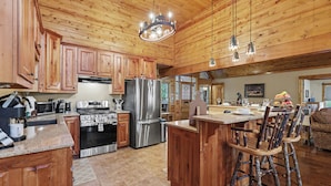 A spacious kitchen with wooden cabinets, stainless steel appliances, and a central island with bar stools. - Vintage Luxury Creekside Cabin ~ King Bed, Hot Tub, Fire Pit & Game Room, Dog Ok (Hiawassee)