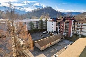 A multi-story hotel with a parking lot, surrounded by mountains and trees. - Gatlinburg. Downtown. 2br (Gatlinburg)