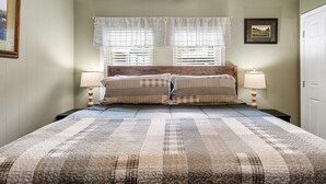 A bedroom with a large bed, two bedside tables with lamps, a window with curtains, and a framed picture on the wall.