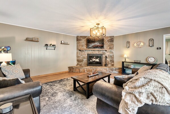 A living room with a stone fireplace, a television above it, and a sofa with a throw blanket. - Gatlinburg. Downtown. 2br (Gatlinburg)