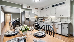 A modern kitchen with white cabinets, a stainless steel refrigerator, and a dining area set for six with a wooden table and chairs.