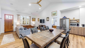 A spacious living area with a wooden dining table, comfortable seating, a kitchen with modern appliances, and a ceiling fan. - Little Bee Woods (Swannanoa)