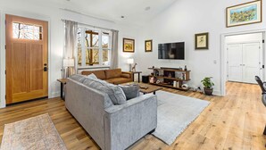 A living room with a grey sofa, a brown leather couch, a wooden coffee table, a TV, and a bookshelf. - Little Bee Woods (Swannanoa)