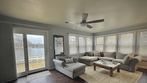 Una sala de estar con un ventanal grande, un ventilador de techo y vistas a un lago.