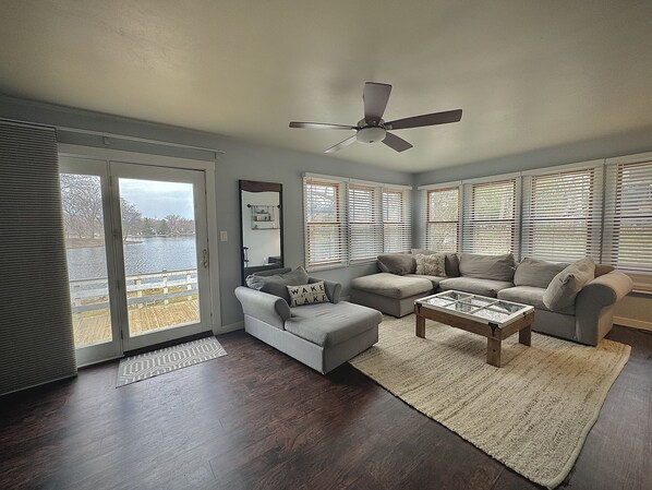 A living room with a large window, a ceiling fan, and a view of a lake.