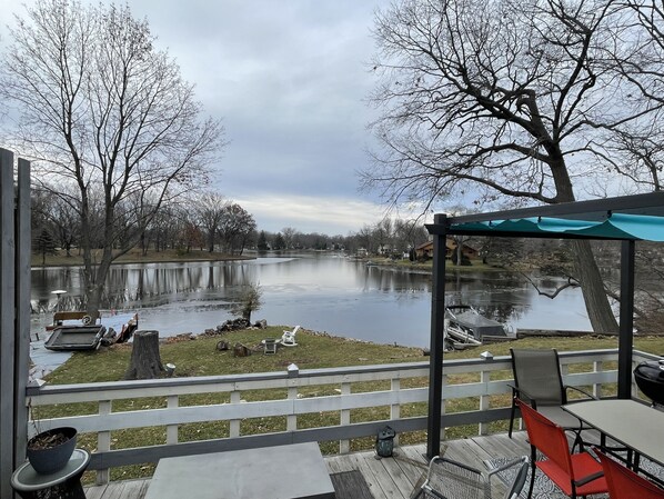 A deck with outdoor furniture overlooking a calm lake, surrounded by trees and a clear sky.
