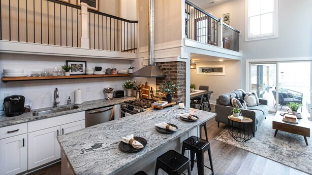 Una cocina moderna con una isla central, un área de comedor con sofá y una escalera que lleva a un nivel superior.