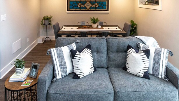 Ein zweistöckiges Haus mit Essbereich, einer Couch mit gemusterten Kissen und einer Treppe mit Geländer.