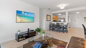 A modern living room with a glass coffee table, a sofa, a TV, and a dining area with chairs and a table. - Cozy 3BR/2BA  King Bed  Free Parking  Pet-Friendly (Miami)