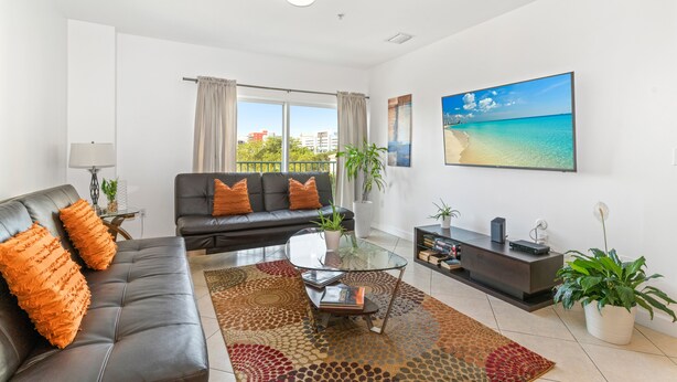 A modern living room with a leather sofa, a glass coffee table, and a large painting of a beach. - Cozy 3BR/2BA  King Bed  Free Parking  Pet-Friendly (Miami)