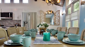 A dining area with a wooden table set with teal-colored dishes and cups, a vase with flowers, and a patterned runner. - The Santi Paradise (Glen Burnie)