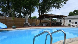 A swimming pool with metal handrails, surrounded by a wooden fence, outdoor furniture, and a covered patio area. - The Santi Paradise (Glen Burnie)