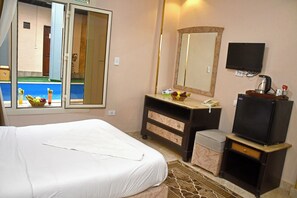 Habitación de hotel con cama, cómoda, espejo, televisión y ventana con vista a la piscina.