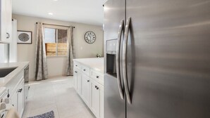 Una cocina moderna con armarios blancos, un refrigerador de acero inoxidable, una ventana con cortinas y un reloj en la pared.