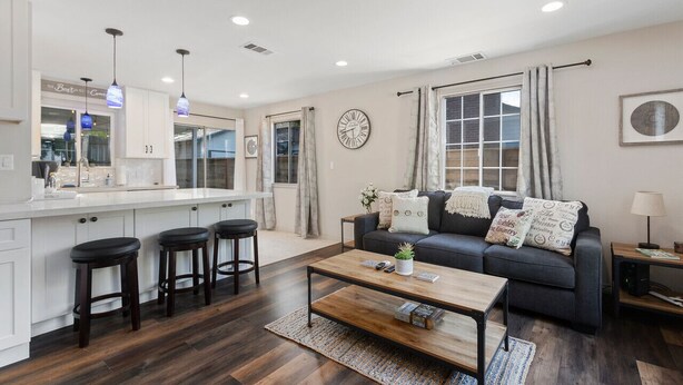 Una sala de estar moderna con un sofá oscuro, una mesa de centro de madera y una zona de cocina con taburetes de bar.