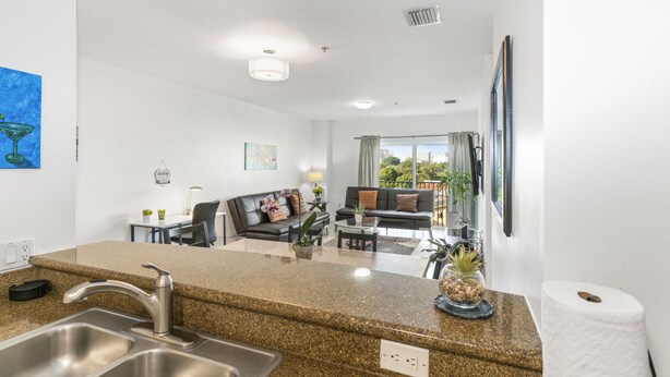 A modern kitchen with granite countertops, stainless steel sink, and a dining area with a black sofa and coffee table. - Stylish 2-Bedroom Apt, Free Parking, Walkable (Miami)