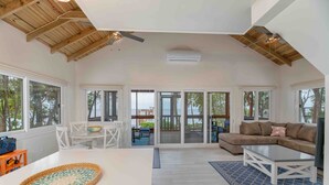Ampla sala de estar com uma janela grande, ventilador de teto e porta de vidro deslizante para um deck externo.