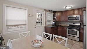 A kitchen with wooden cabinets, a microwave, a stove, and a dining table with chairs. - Perfect spot! Cape Cod -1 block to beach and bay with views! (Beach Haven)