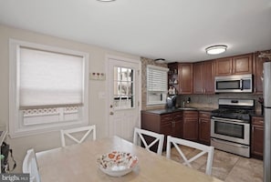 A kitchen with wooden cabinets, a microwave, a stove, and a dining table with chairs. - Perfect spot! Cape Cod -1 block to beach and bay with views! (Beach Haven)