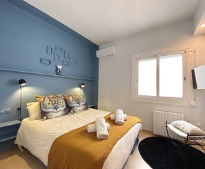 Een slaapkamer met een bed, twee bedlampen, een raam, een radiator en een televisie aan de muur.