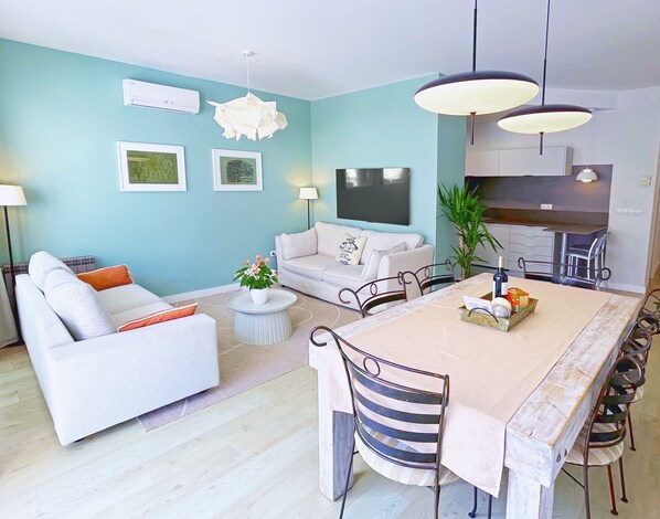 Een moderne woonkamer met een bank, een eettafel met stoelen, een televisie en een keukenhoek.