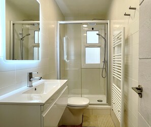 Een moderne badkamer met een douchecabine van glas, een witte wastafel en een toilet.